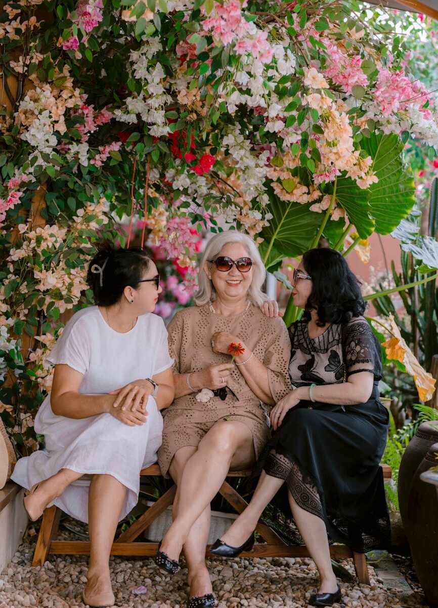 three women enjoying a garden bench under colorful blooms