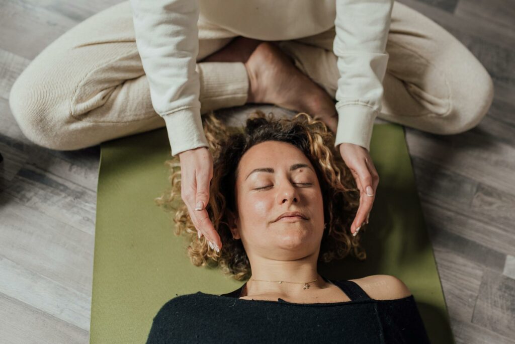 Frau liegt entspannt auf einer Yogamatte, während eine Person ihren Kopf sanft hält